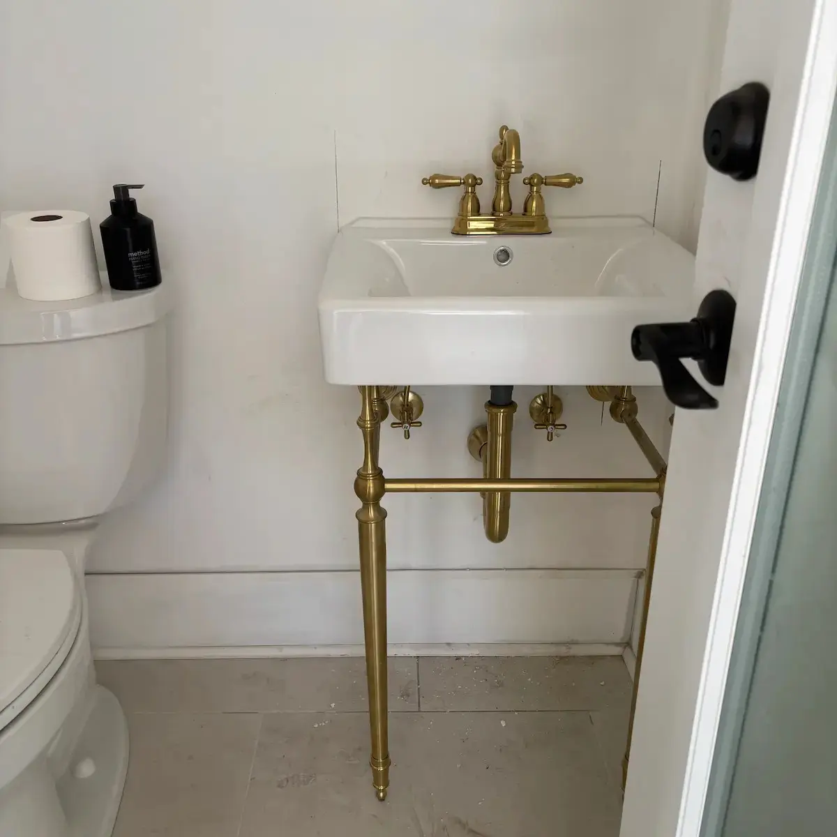 A white porcelain console bathroom sink with vintage-style polished brass legs and faucet fixtures next to a white toilet.